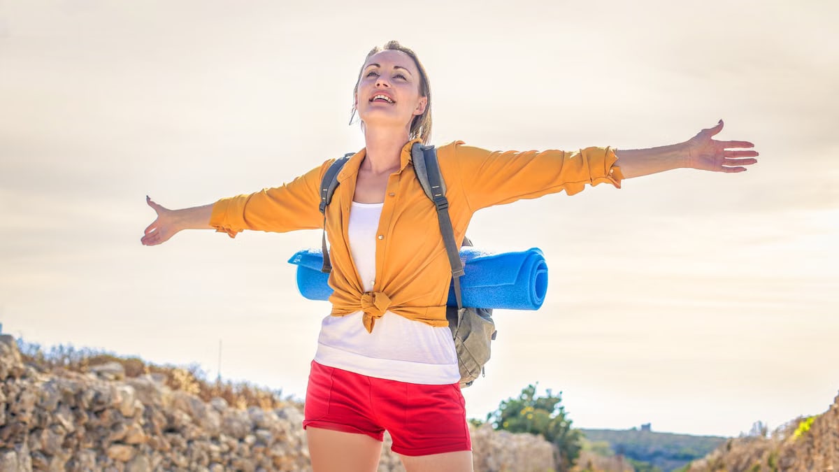 Happy woman basking in sunlight on a summer hike with yoga mat.